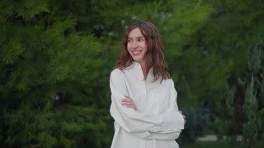 Ağaçların arasında dikilen pozitif, mutlu esmer genç bir kızın portresi. Kendine güvenen güzel bir kadın gülümsüyor ve çapraz kollarla kameraya bakıyor. Öz bakım ve sevgi Farkındalık Doğal güzellik 