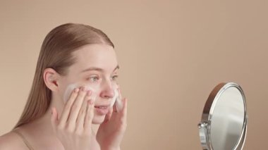 Cilt bakımının keyfini çıkaran genç ve güzel bir kadın gülümseyerek nazikçe köpük temizleyici sürüyor. Sabah güzellik ayini, temiz ve az estetik. Yüz temizleme köpüğü reklamı konsepti.