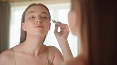 Genç bir kadın aynanın önünde rimel sürüyor. Kendine güvenen ve odaklanmış bir şekilde, günlük makyaj rutininin bir parçası olarak kirpiklerini büyütüyor. Rimel ürünü reklamı ve güzellik içeriği kavramı.