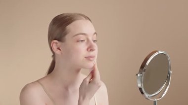Genç bir kadın sabah cilt bakımı sırasında yüzünü pamukla nazikçe temizliyor. Minimalist kişisel bakım ritüeli, sağlıklı ve ışıl ışıl bir cilt. Doğal güzellik ve evde nazik yüz bakımı..