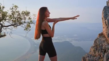 Spor kıyafetleriyle ısınan bayan sporcu dışarıda spor yapmaya hazırlanıyor. Gün batımında doğada koşmadan önce kollarını ve vücudunu esneten genç bir kadın. Fiziksel egzersiz. Sağlık, motivasyon..