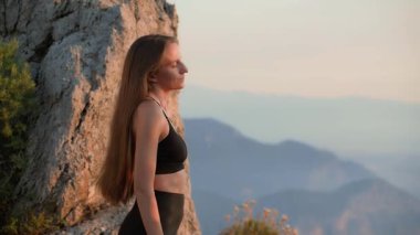 Gün batımında doğada boyun esnetme egzersizleri yapan zinde genç bir kadın. Duruş, kas gevşeme ve esneklik için açık hava ısınma rutini. Sağlıklı yaşam tarzı ve spor giyim sektöründe kişisel bakım..