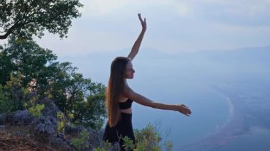 Genç bir kadın sabah huzurlu bir ortamda ısınıyor ve kollarını açıyor. Açık hava fitness, hareketlilik, farkındalık, sağlıklı yaşam tarzı kavramı. Sağlıklı kadın dışarıda egzersiz yapıyor.