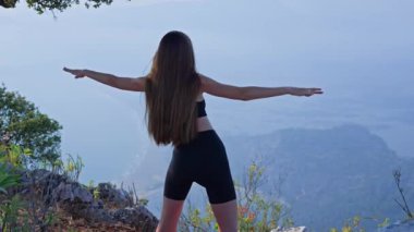 Kollarını uzatan ve doğada ısınan genç bir atletik kadının arka plan görüntüsü. Açık hava hareketlilik eğitimi, dışarıda çalışma, dinlenme, farkındalık, fitness eğitimi, sağlıklı yaşam tarzı.