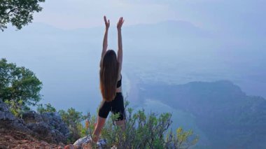 Genç bir kadının kollarını kaldırışının arka görüntüsü. Pilates, Fitness. Enerji, özgürlük, berraklık, başarı ve içsel güç kavramı doğadaki bilinçli hareket yoluyla