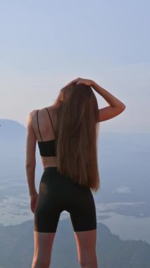 Gün batımında boynunu dışarı uzatan atletik bir kadının görüntüsü. Sportif genç yetişkin ısınıyor ve kişisel bakım için dinleniyor. Duruş, esneklik, sağIık için yaz egzersizi