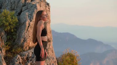 Spor kıyafetli genç bir kadın yazın günbatımında dışarıda omuz ısıtması yapıyor. Yüzünde hafif bir gülümseme vardı. Akşam antrenmanından önce esneme hareketleri. Hareket, denge ve refah kavramı.