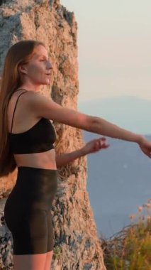 Spor giyim sektöründe aktif bir kadın akşam antrenmanından önce gün batımında kollarını açık havada açıyor. Bilinçli hareket kavramı, güç, doğadaki refah. Sportif kız ve ısınma egzersizi..