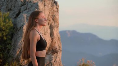 Calm young woman practicing deep breathing after workout outdoors at sunset. Peaceful recovery and relaxation in nature. Concept of Mindfulness, Wellness, Mental Well-being, and Healthy lifestyle