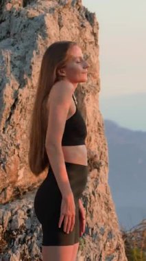 Spor giyimli genç ve formda bir kadın yazın günbatımında dışarıda omuz ısıtması yapıyor. Yüzünde hafif bir gülümseme vardı. Akşam antrenmanından önce esneme hareketleri. Hareket, denge, refah kavramı