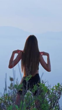 VERTICAL VIDEO sabah kollarını ve omuzlarını dışarı uzatan sportif genç bir kadının arka görünümü. Atletik kadın doğada ısınıyor. Zindelik, sağlık, esneklik, sağlıklı yaşam tarzı kavramı