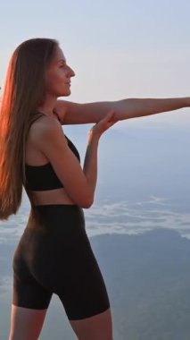 Spor giyimde ısınan bayan sporcu, açık hava fitness antrenmanına hazırlanıyor. Gün batımında kollarını ve vücudunu esneten genç ve zinde bir kadın. Fiziksel egzersiz. Sağlık, motivasyon..