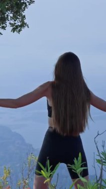 VERTICAL VIDEO Genç kadın dikkatli üst vücut hareketleri ve nefes çalışması yapıyor sessiz doğal bir ortamda sabah, arka manzara. İyileşme kavramı, hareketlilik, kişisel bakım, doğayla bağlantı