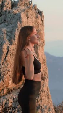 VERTICAL VIDEO Atletik kadın gün batımında omuz ısıtma gösterisi yapıyor. Sportif bir kız ve doğada bir akşam sporu. Güç, denge, kuyu kavramı. Eklem ve kas hasarının önlenmesi