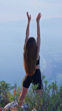 Açık havada bir sabah esnemesi sırasında kollarını kaldıran genç bir kadının arka görüntüsü. Pilates, Fitness. Enerji, özgürlük, berraklık ve içsel güç kavramı doğadaki bilinçli hareket yoluyla