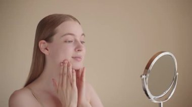 Genç bir kadın gülümseyerek tenine dokunarak cilt bakımının sonucuna hayran kalır. Doğal bir görünüş, sağlıklı parlayan bir ten, rahat ve tatmin edici bir ifade. Güzellik ve özgüven kavramı.