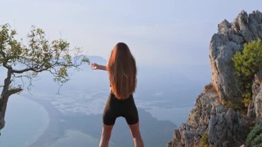 Spor yapan genç bir kadın antrenmandan önce gün batımında omurga bükümü yapıyor. Esnekliği artırmak ve duruşunu geliştirmek için açık hava ısınması. Dikkatli nefes alma ve sağlıklı dönüş kavramı.