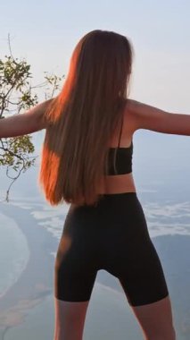 Gün batımında ısınma turunda kollarını yan yana tutan sportif bir kız. Omuzları çalıştırmak ve duruşunu geliştirmek için nazikçe esne. Güç, nefes ve denge kavramı.