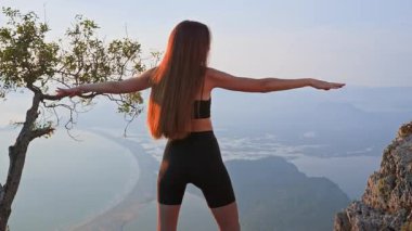 Gün batımında ısınma turunda kollarını yana doğru uzatan sportif kız. Omuzları çalıştırmak ve duruşunu geliştirmek için nazikçe esne. Güç, nefes ve denge kavramı.