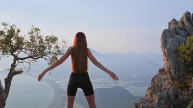 Spor kıyafetli bir kadın gün batımında, arka planda omuz hareketlerinde yavaş hareket ediyor. Eklem esnekliği ve yaralanma önleme için hafif bir ısınma. Sağlıklı hareket ve aktif eğlence kavramı.