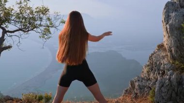 Spor kıyafetli bir kadın gün batımında ısınma turu sırasında kollarını yanlara uzatarak gövdesini çeviriyor. Hareket kabiliyeti, omurilik kontrolü ve dengeli hareket kavramı. 