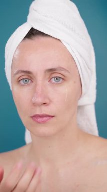 VERTICAL VIDEO Estetik kadın cilt için hidratlaştırıcı yüz serumu kullanarak cilt parlamasını arttırmak ve cilt modelini Stüdyo Mavi Arkaplan Dermatoloji Yüzlü Serum reklamında dönüştürmek için kozmetik uygula
