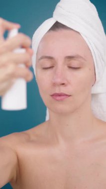 Dikey video. Pretty Woman Yüz Spreyi Spreyi Spreyliyor ya da Termal Su Yüzlü Toner Yüz Spreyi Yavaş Çekimde Spreyliyor. Tonlama ferahlatıcı nemlendirici yüz derisi. Stüdyo Mavi Arkaplan.