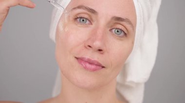 Cilt bakımı için hidratasyon serumu kullanan bir kadın parıltıyı arttırmak ve ten rengini değiştirmek için kozmetik ilaçlar kullanıyor. Stüdyoda mankenlik, yüz güzelliği için hiyalüronik asidin cilt bakımı yararları. Gri arkaplan