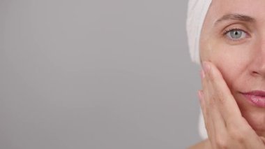 Yarı kadın yüzünün yakın plan portresi, yüzüne serum süren ve stüdyoda kameraya bakıp gülümseyen kadın. Gri arka plan. Cilt bakımı için reklam konsepti, güzellik kozmetiği. Boşluğu kopyala.