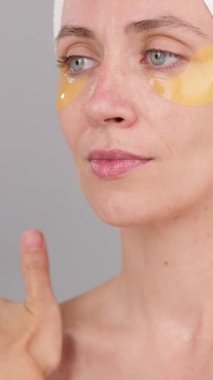 Dikey video: Gri arka planda, gençleştirici nemlendirici krem ve masaj tasması takan genç, beyaz, güzel bir kadın. Vücut Bakımı Rutin Spa