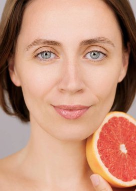 Greyfurt, gri arkaplan, doğal cilt bakımı, C vitamini ya da detoks içeren güzel beyaz kadın. Stüdyo portresi, çevre dostu kozmetik ürünler, organik beslenme