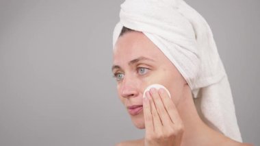 Cilt bakımı. Cotton Round ya da Cotton Pad kullanan beyaz bir kadın stüdyo arka planında yüzünü temizliyor. Gülümseyen bir model portresi, günlük kişisel bakım. Ağır çekim. Dermatoloji yüz tedavisi