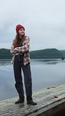 Finlandiya 'da bir orman gölünün kıyısındaki ahşap iskelede tek başına duran genç bir turist kadının görüntüsü. Doğayı, sessizliği seviyor. Dikkatli seyahat kavramı, eko-turizm, barışçıl keşif