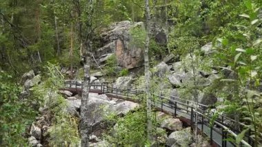 Wide view of a modern elevated metal walkway above a rocky hill in a Finnish forest. Concept of eco friendly tourism, accessible nature trails, and Nordic integration of design and wilderness. Lapland