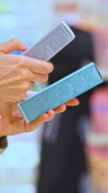VERTICAL VIDEO Woman güzellik mağazasında yüz veya saç için kozmetik serumu seçiyor ve malzemeleri okuyor, ürünleri karşılaştırıyor. Cilt bakımı ya da saç bakımı malzemesi tutan kadın müşteri. Bilinçli seçim