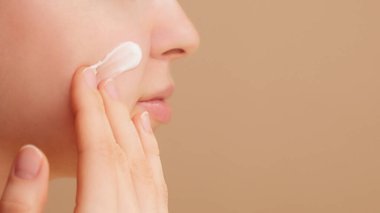 Yüzünün yarısı tanınmayan bir kadın portresi nemlendirici krem sürüyor, güneş kremi sürüyor, makyaj hazırlıyor. Güzellik rutini reklamları. Cilt bakımı reklamı. Kişisel bakım. Stüdyo çekimi. Güzellik merkezi. Boşluğu kopyala