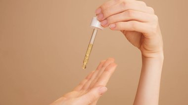 İzole edilmiş bej arka plan tutucu, yaşlanma önleyici yüz serumu, avuç içine damlayan güçlendirici. Ticari cilt bakımı, nemlendirici, C vitamini, kırışıklık önleyici reklamlar.