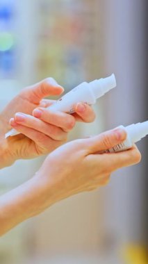 Bir kozmetik mağazasında nemlendirici SPF kremi seçen, cilt bakım ürünlerini ve makyaj ürünlerini karşılaştıran, malzeme etiketlerini okuyan kadın müşteri. Kadınların ellerinin iki tüp tuttuğu yakın plan..