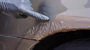 Pas hasarını inceleyen ve araba yüzeyindeki boyaları soyan eldivenli bir elin yakın çekimi. Araç denetimi, hasar değerlendirmesi, sigorta talepleri ve aşınma teşhisi konsepti.