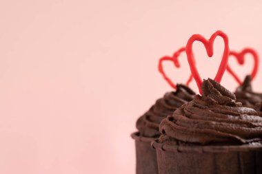 Chocolate cupcakes with ganache frosting and a red heart on each on a pink background