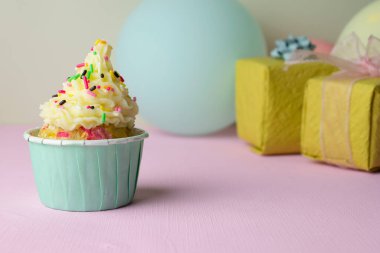 Tereyağlı kremalı pasta ve pembe arka planda hediyeler ve balonlarla kaplı renkli şekerlemeler.
