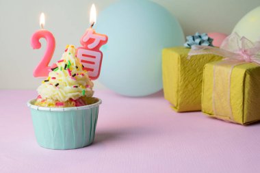 İki aylık mumları olan, etrafında balonlar ve pembe arka planda hediyeler olan bir doğum günü pastası.