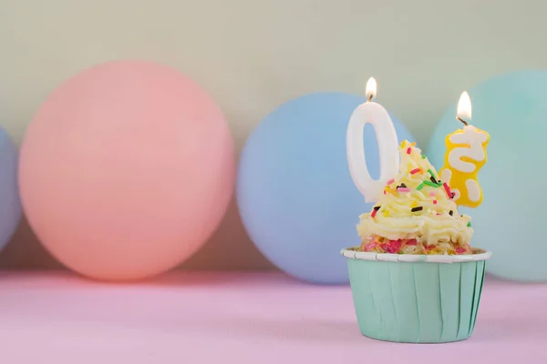 ピンクの背景に風船で囲まれた0年のキャンドルの誕生日カップケーキ — ストック写真