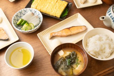 Izgara somon, pirinç, Japon omleti, tabakta turşu ve ahşap masada kase ile Japon tipik kahvaltı seti..