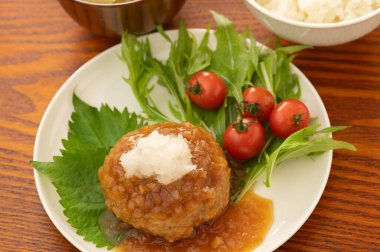 Bir tabak kiraz domatesli ve yeşil yapraklı Japon hamburger bifteği ve üstüne de jöleli turp ve soya sosu.