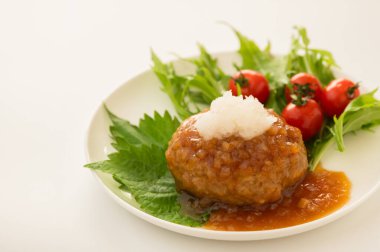Çeri domatesli ve yeşil yapraklı bir tabakta Japon hamburger bifteği ve üzerine de jöleli turp ve soya sosu.