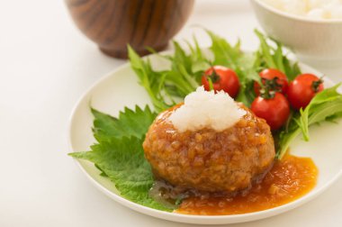 Çeri domatesli ve yeşil yapraklı bir tabakta Japon hamburger bifteği ve üzerine de jöleli turp ve soya sosu.