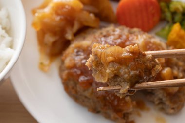 Japon hamburgerinin soğan soslu bifteğinin sotelenmiş sebzeli bir ısırığının yakın çekimi..