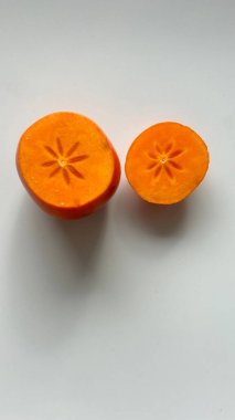 Açık arkaplanda dilimlenmiş parlak turuncu hurmalar benzersiz şekillerini sergiliyorlar.