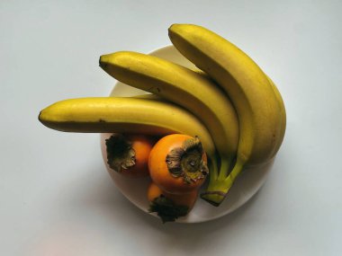 Doğal ışıklandırmada hafif bir yüzey üzerinde olgun muz ve hurma kasesi.